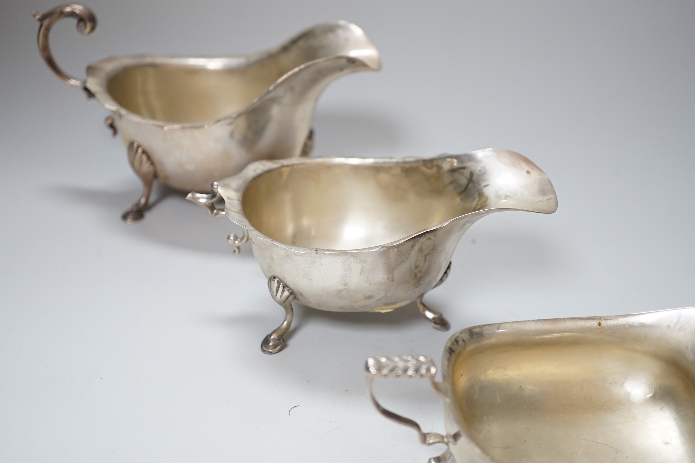 A George V silver sauceboat, Chester 1915, 189 grams, a later sauceboat with damaged handle, 82 grams and a shallow rectangular form sauceboat, 76 grams